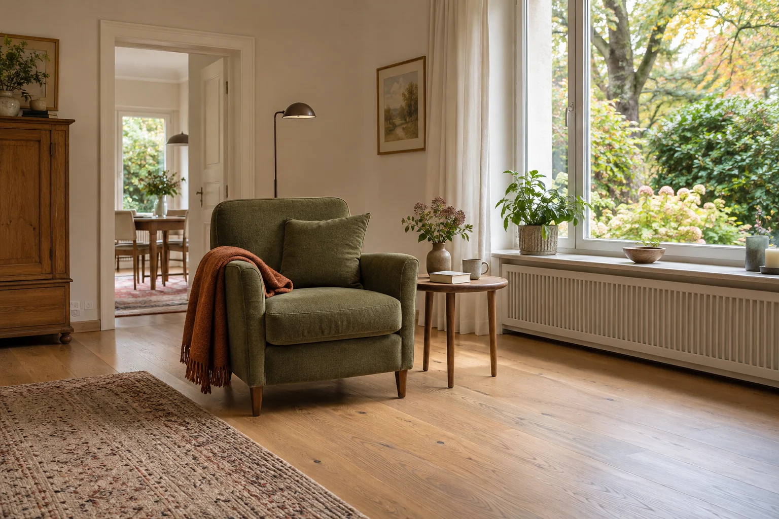 Olivgrüner Sessel mit rostfarbener Decke neben einem Beistelltisch mit Buch und Tasse; dahinter liegt ein grüner Garten.